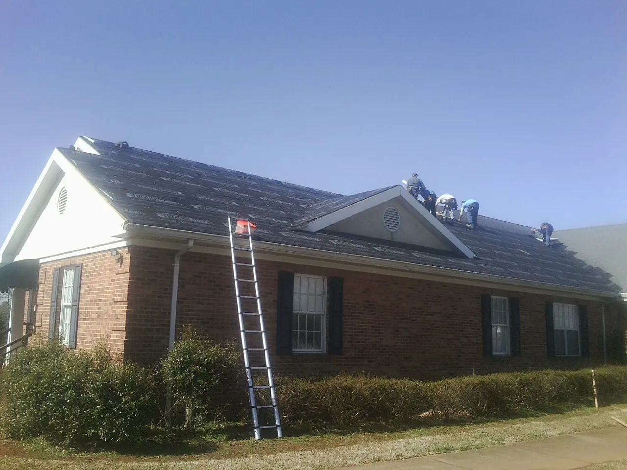 Crew tearing shingles off a brick ranch roof with a ladder set — Emergency Roof Repair work by our crew in Marianna