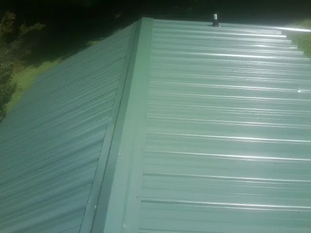 New green metal panels meeting at the ridge of a roof — Flat Roof Repair work by our crew in Marianna