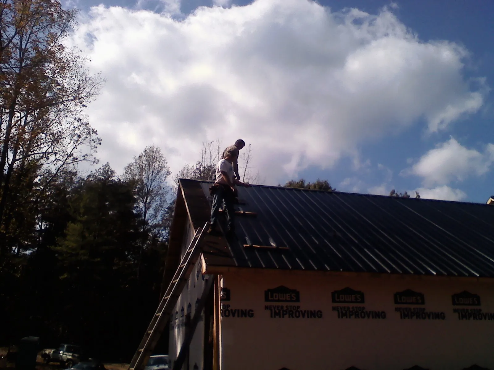 Roofer fastening dark metal panels high against a cloudy sky, from a Roof Inspection job in Marianna