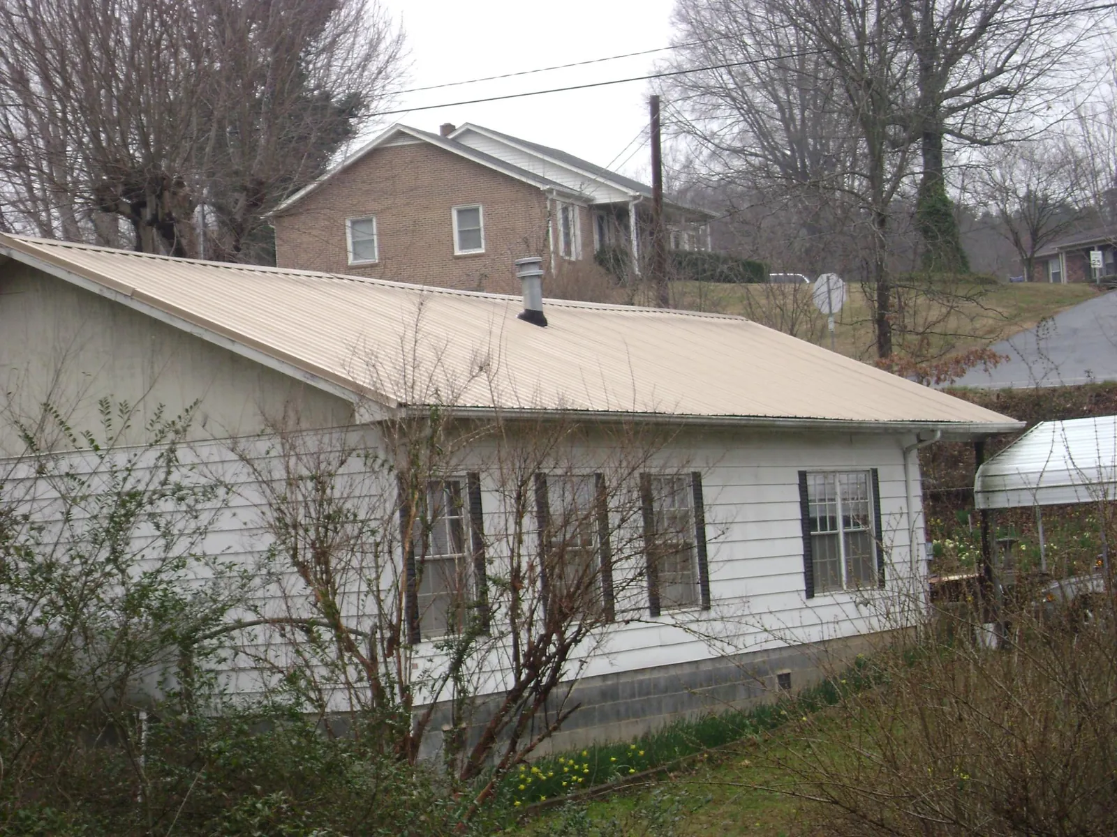 Tan metal roof on a white sided house set into a hillside — Commercial Roofing by Roofing Brothers in Marianna