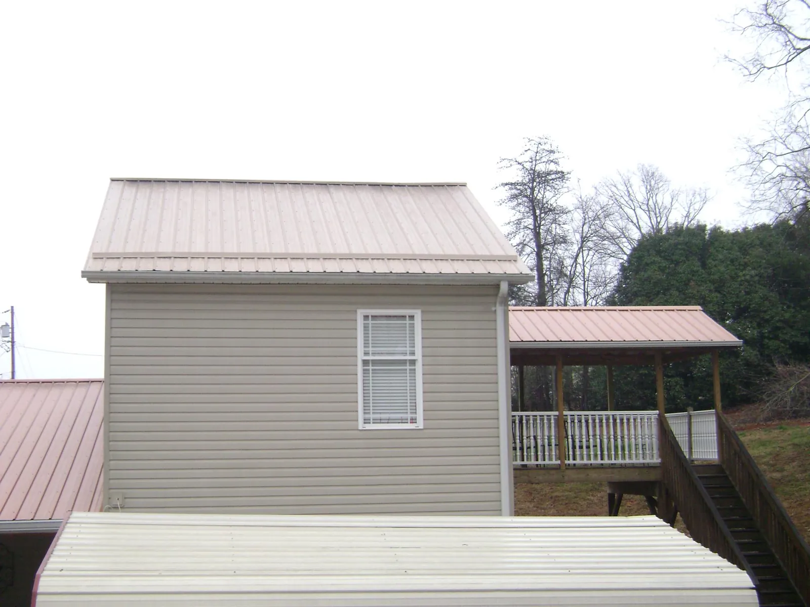 Tan metal roofs on a two story addition and attached porch, from a Roof Replacement job in Marianna